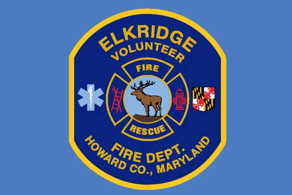 A circular patch with a gold trim displays "Elkridge Volunteer Fire Dept. Howard Co., Maryland" around a rescue emblem. The emblem contains a medical symbol, a ladder, a deer, a fire hydrant, and the Maryland flag against a blue background.
